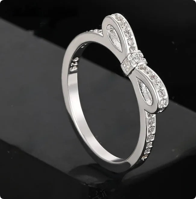 Silver bow-shaped ring with crystal zircon and rhinestone detailing on a finger