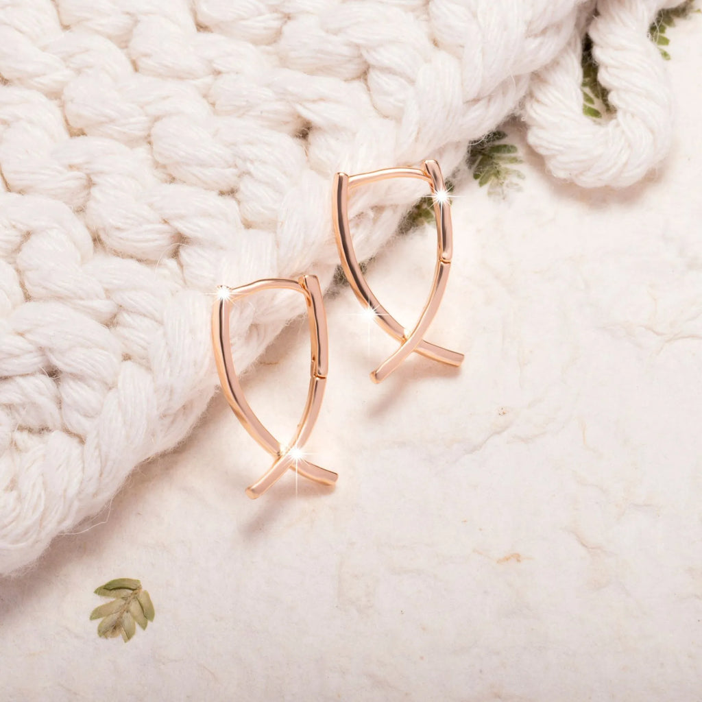 A pair of rose gold plated copper earrings in a cross shape on a plain background.