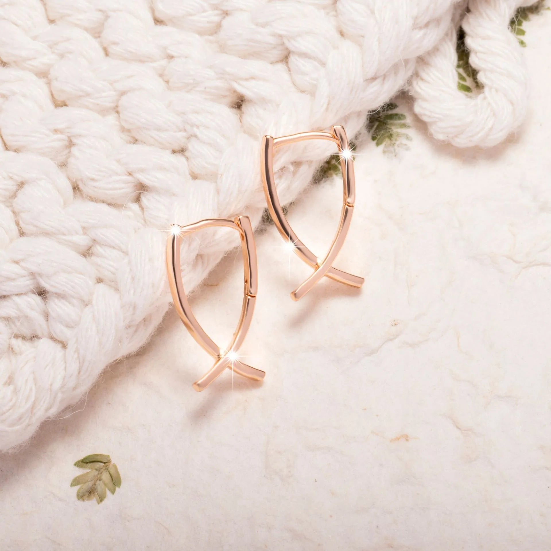 A pair of rose gold plated copper earrings in a cross shape on a plain background.