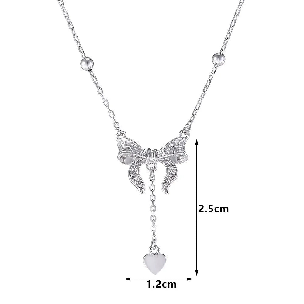 A close-up of a silver necklace with a heart and bow pendant on an O-ring chain.