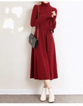 A woman wearing a rose red turtleneck long-sleeve knit dress with an elastic waist and loose hem.