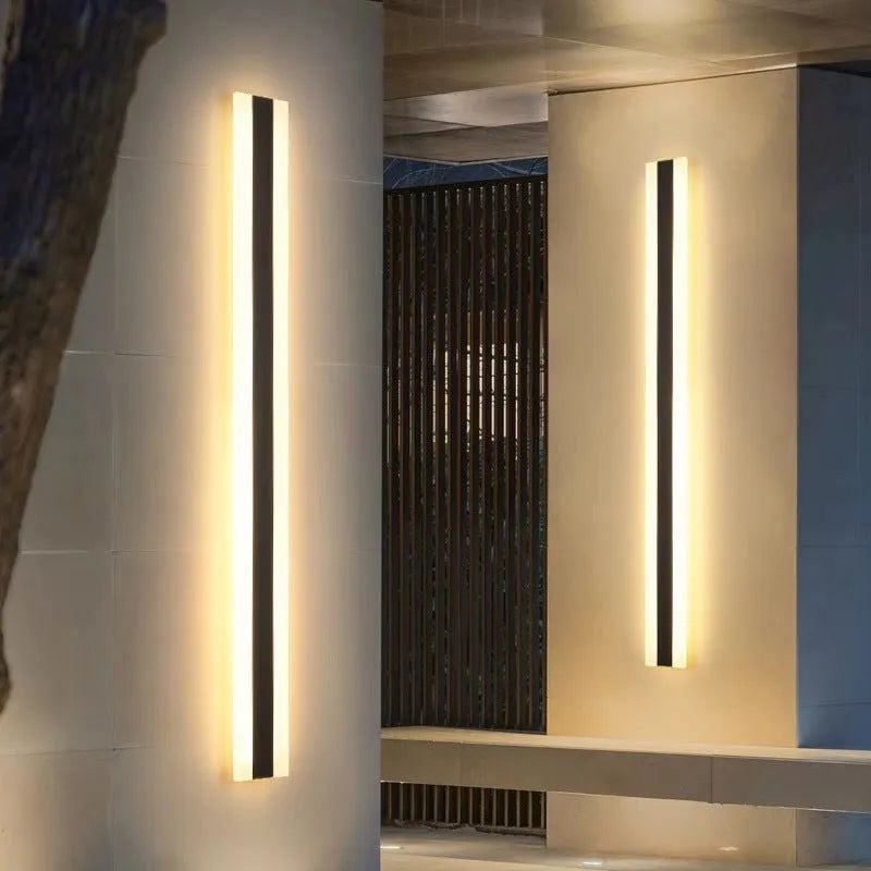 A long, straight outdoor LED wall lamp with a black wrought iron shell, mounted on a brick wall.