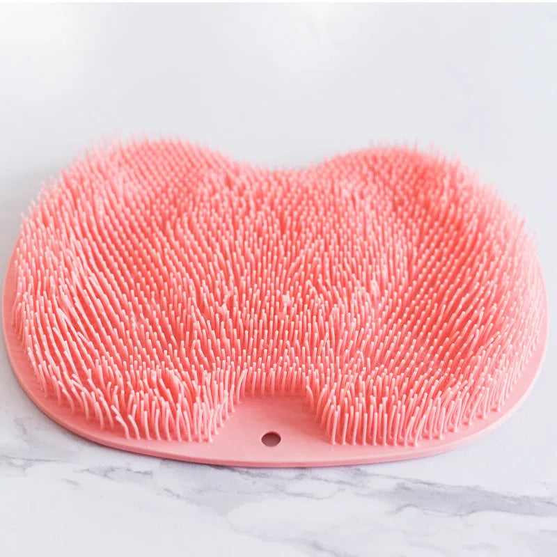 Orange massage bath brush with silicone bristles and suction cup base on a shower floor
