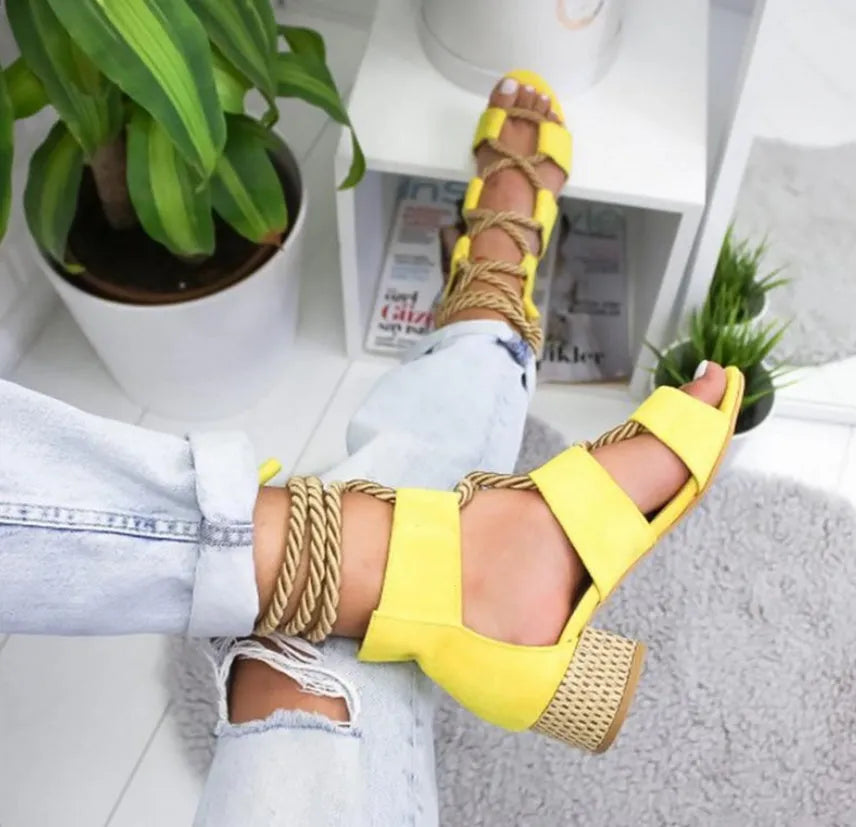 Women's beige suede sandals with thick middle heel, front strap, and ankle strap on a neutral background.