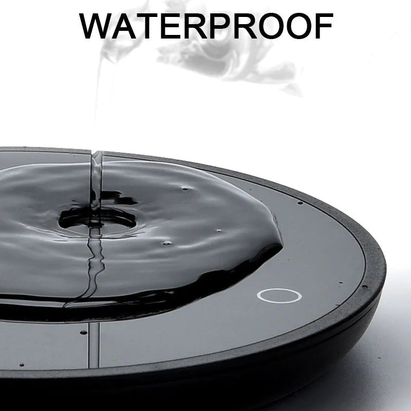Black circular mug warmer with temperature switch, 12cm in diameter, on a desk next to a coffee cup.