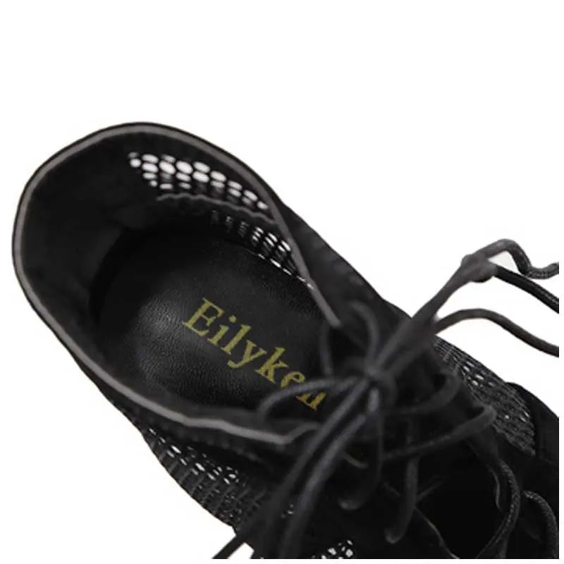 Black suede women's lace-up high heel shoes with a tall heel on a wooden floor.