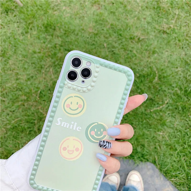 Green TPU iPhone case with geometric smiley face and polka dot design on a table.