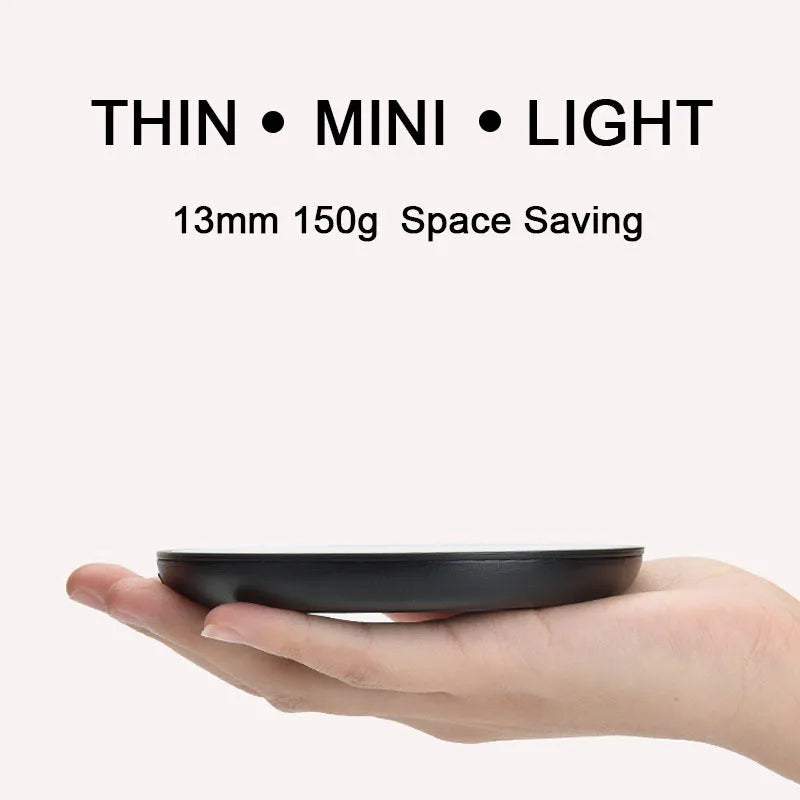 Black circular mug warmer with temperature switch, 12cm in diameter, on a desk next to a coffee cup.