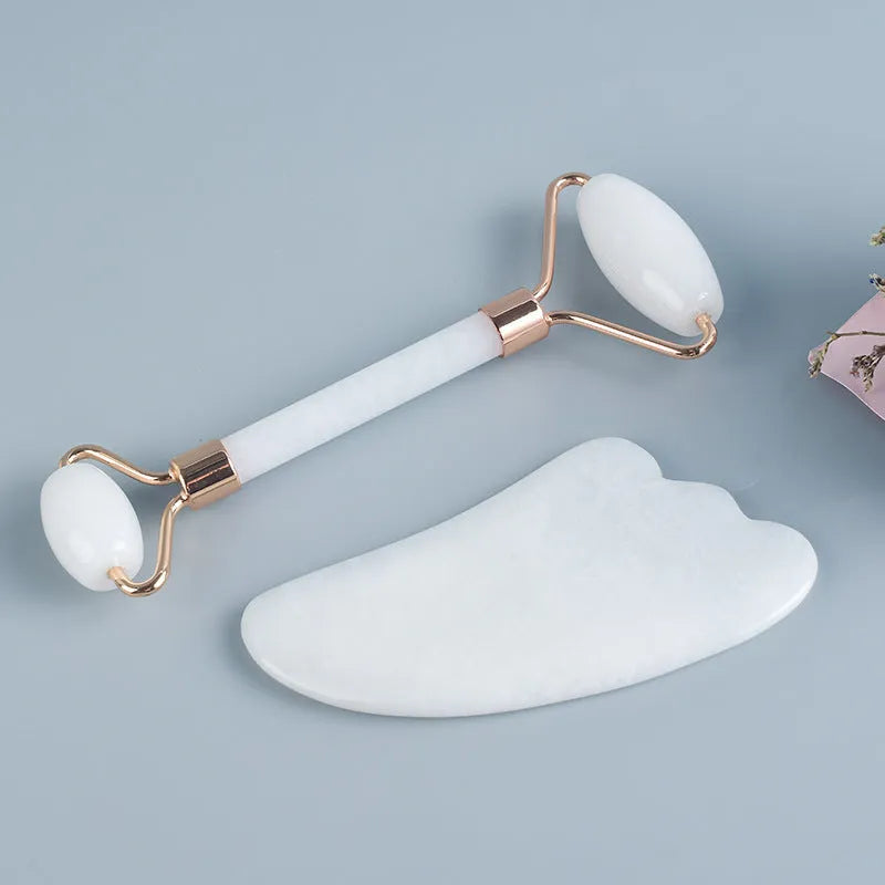 White jade facial roller and Gua Sha scraping board set on a plain surface.