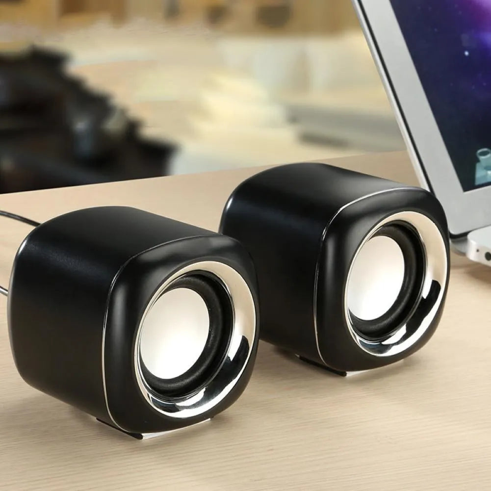 Pair of black wired mini desktop computer speakers with 3.5mm plug and scroll wheel volume control on a desk