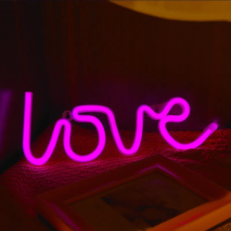 Pink Love-shaped LED neon sign light on a table with battery and USB power options