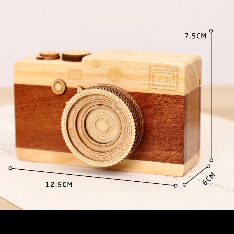 Pine wood camera-shaped music box with rotating mechanism on a wooden surface.