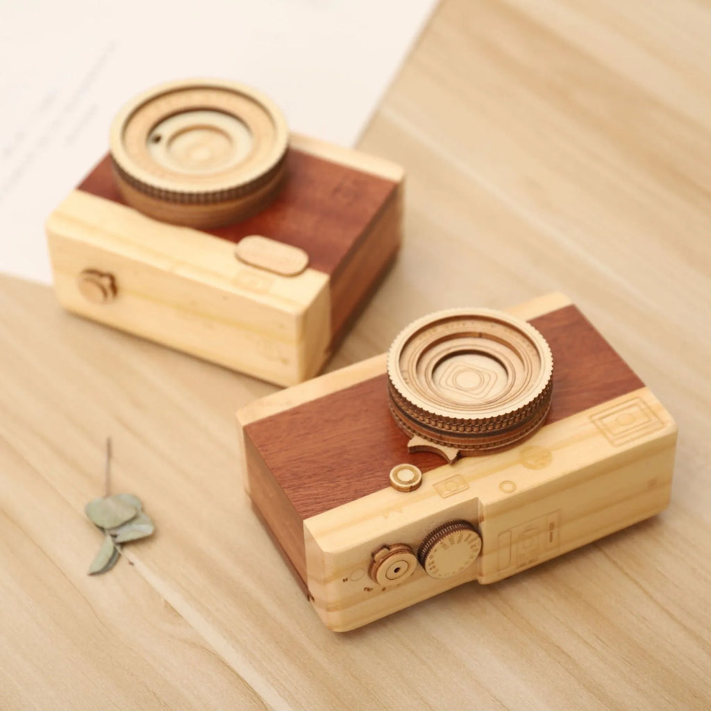 Pine wood camera-shaped music box with rotating mechanism on a wooden surface.