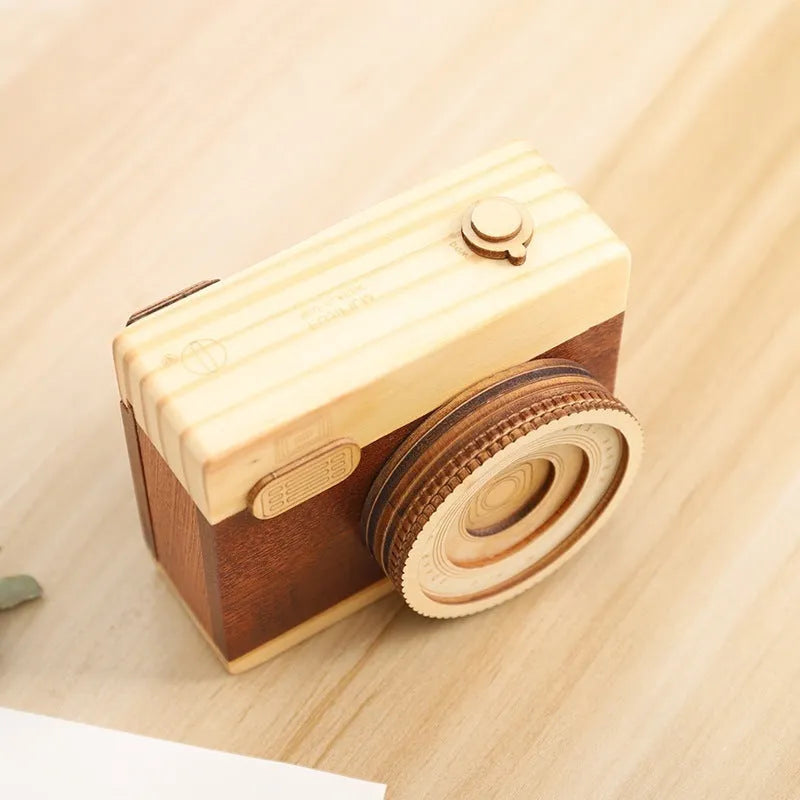 Pine wood camera-shaped music box with rotating mechanism on a wooden surface.