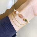 Close-up of a women's geometric bracelet with pink freshwater pearls and strawberry crystals on a wrist.