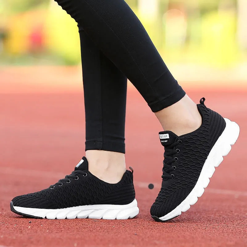 Women's running shoes in black, pink, and white with a fly weave upper and durable outsole.