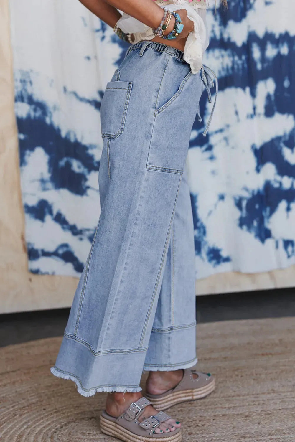Beau Blue colour wide leg denim trousers with a drawstring waist and raw hem seam detail laid flat.