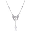 A close-up of a silver necklace with a heart and bow pendant on an O-ring chain.