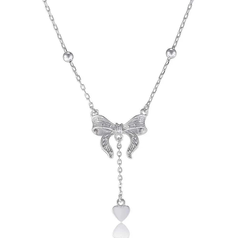 A close-up of a silver necklace with a heart and bow pendant on an O-ring chain.