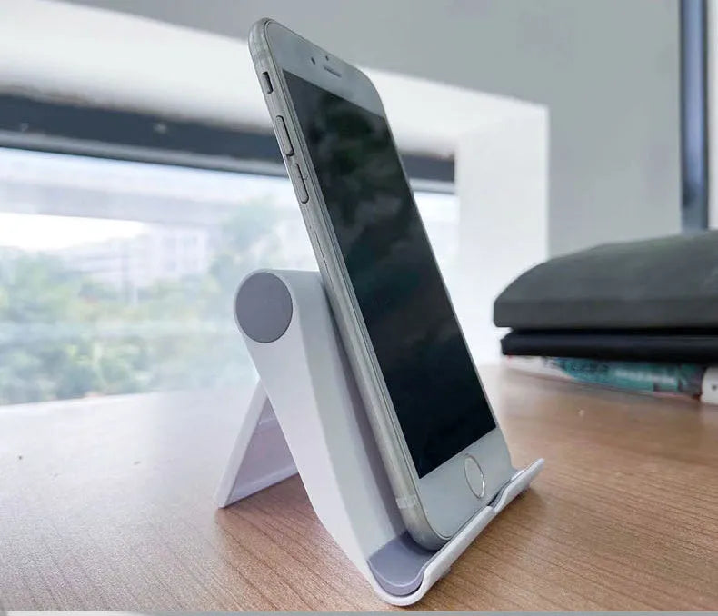 Black PE plastic folding phone stand holding a mobile phone at an angle on a wooden desk.