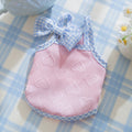 Small dog wearing a blue elastic vest with heart texture, suspenders, and a bow.