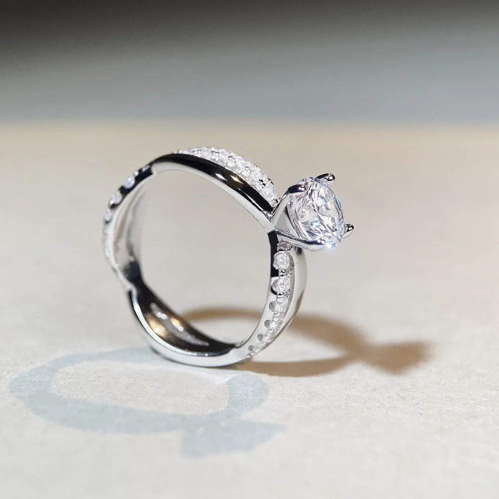 Close-up of a silver ring with a 1 karat moissanite in a four-claw setting, geometric cross design, and twisted band.