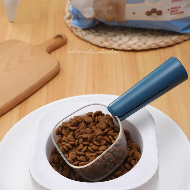Transparent plastic pet food spoon with scale markings for measuring cat and dog dry food, available in Blue Pink White