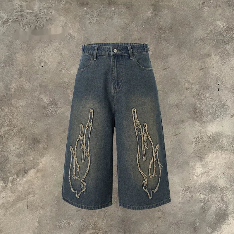 Men's black cropped denim shorts with red and orange patch flame embroidery on the leg.