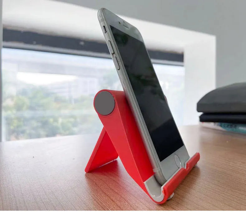 Black PE plastic folding phone stand holding a mobile phone at an angle on a wooden desk.