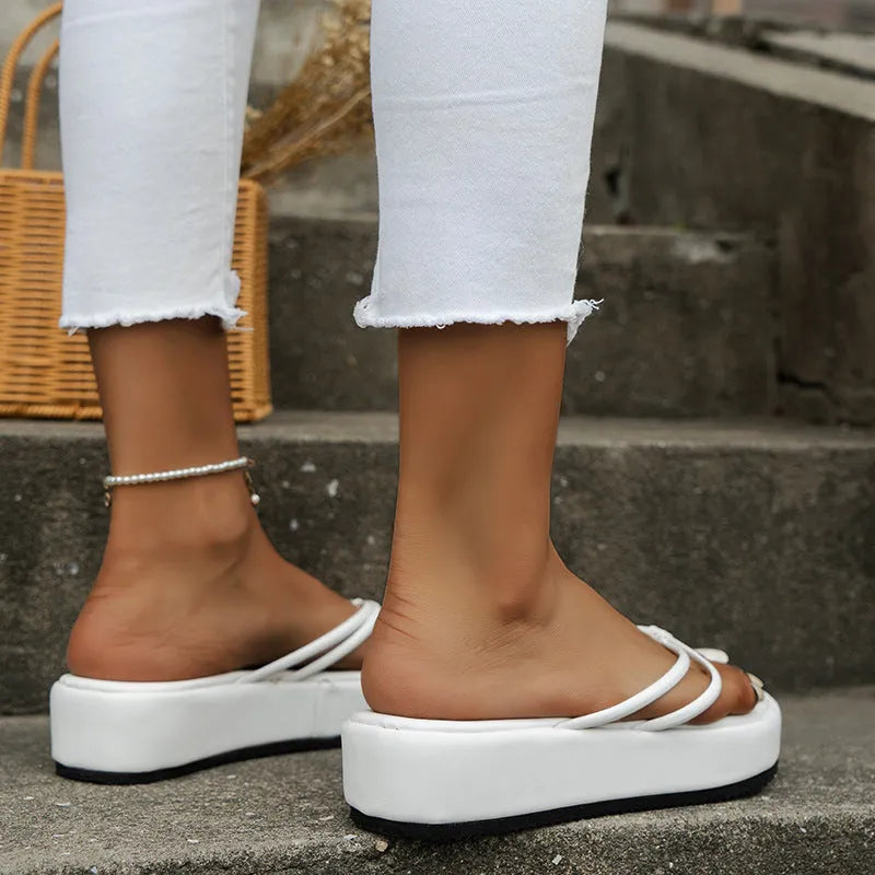 White herringbone-pattern flip-flops with a thick rubber sole on a sandy beach background.