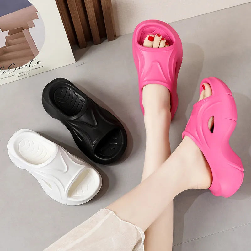 Women's white thick-soled EVA slippers with round toe on a sandy beach.