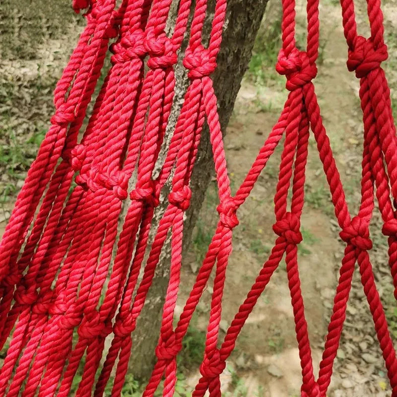 Nylon rope mesh hammock hung between two trees in a garden setting.