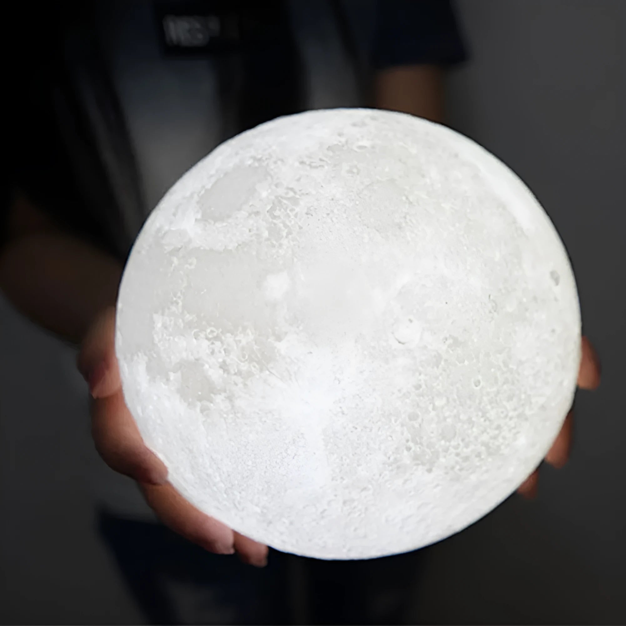 3D printed white moon lamp on a wooden stand with a glowing centre.