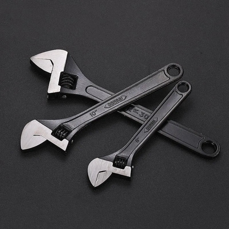 Blackened high carbon steel adjustable open-end wrench on a workbench, jaw set to mid-opening.