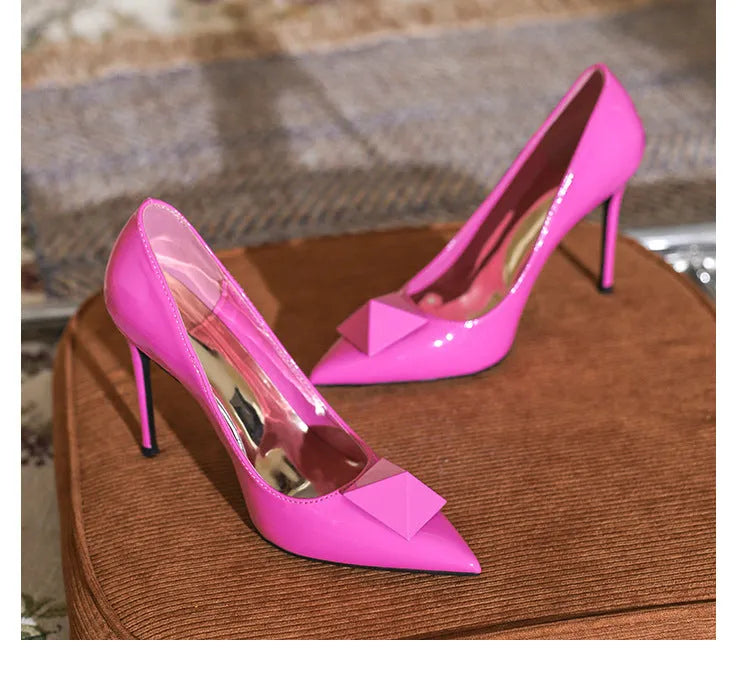 Pink patent leather women's stiletto heels with pointed toes and rivet buckle detailing