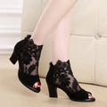 Black lace gladiator sandals with a square high heel, floral detail, and a zip closure at the ankle.