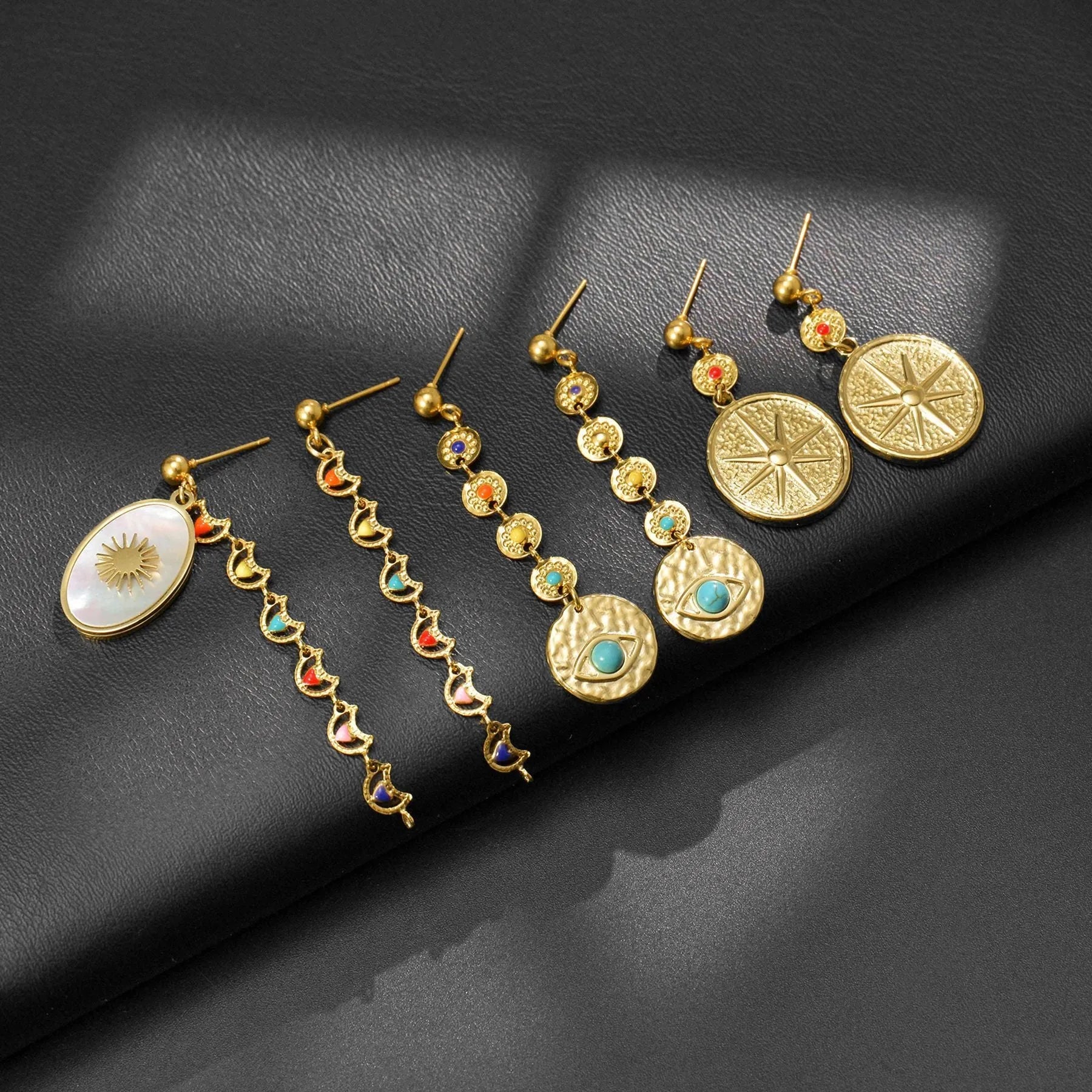 Three pairs of geometric stainless steel earrings on display: Eight Awn Star, Eye, and Shell Sun designs.