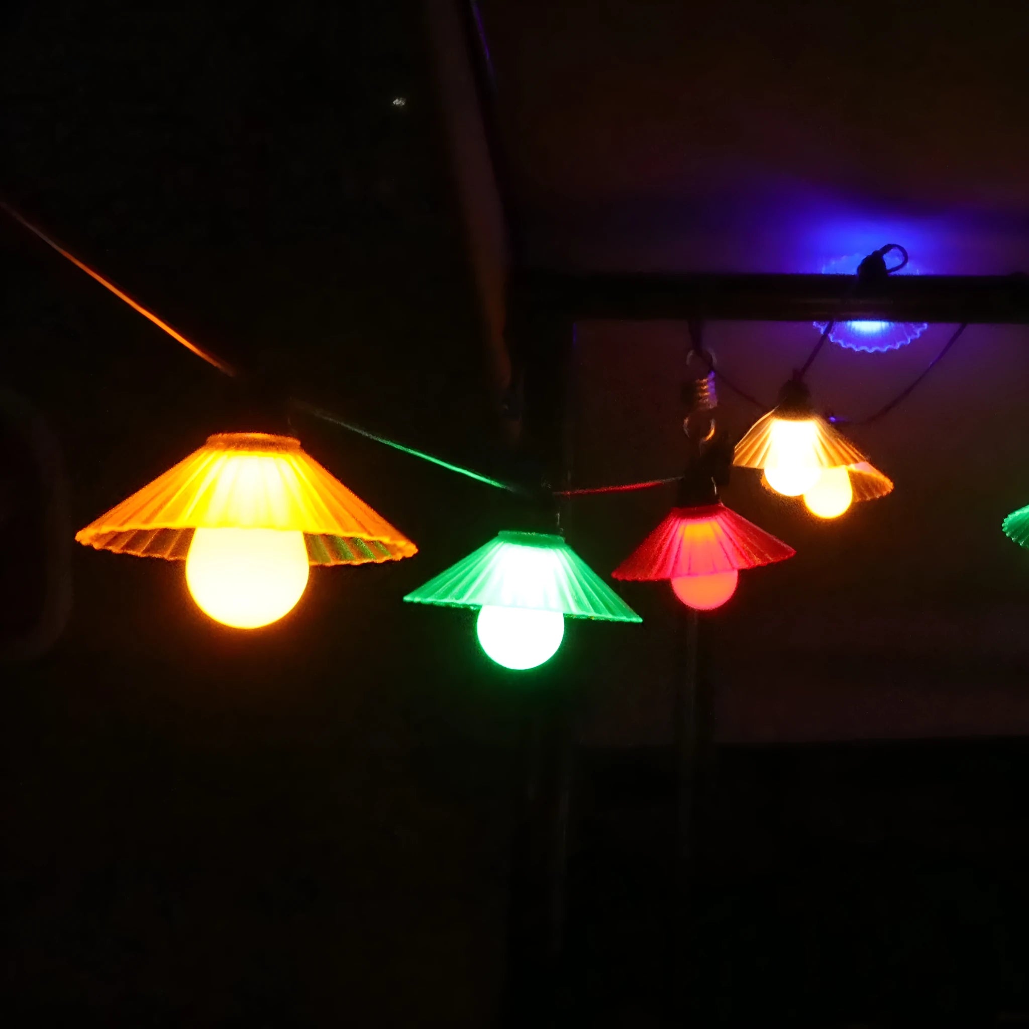 Outdoor LED string lights with flower-shaped globes in four colours, hanging in a garden.