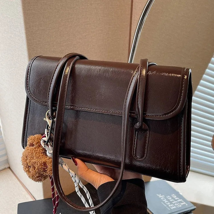 Brown women's PU leather square shoulder bag with double straps and a matching tassel pendant on a table.