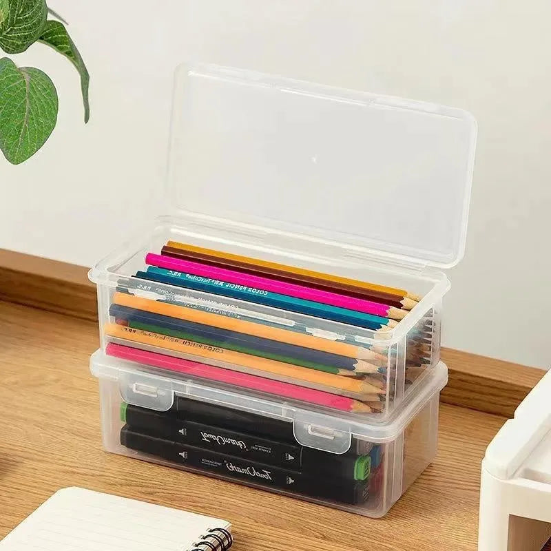Clear plastic stationery storage box full of coloured pencils and drawing tools on a table.