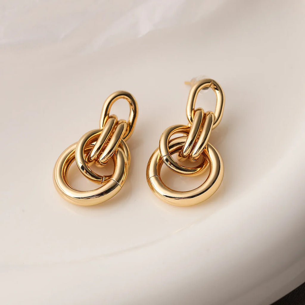 A pair of gold geometric drop earrings with an irregular asymmetric shape, made from copper.