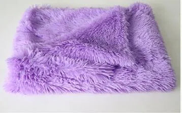 Soft long plush dog blanket in dark grey, shown on a floor next to a pet kennel.