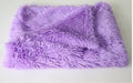 Soft long plush dog blanket in dark grey, shown on a floor next to a pet kennel.