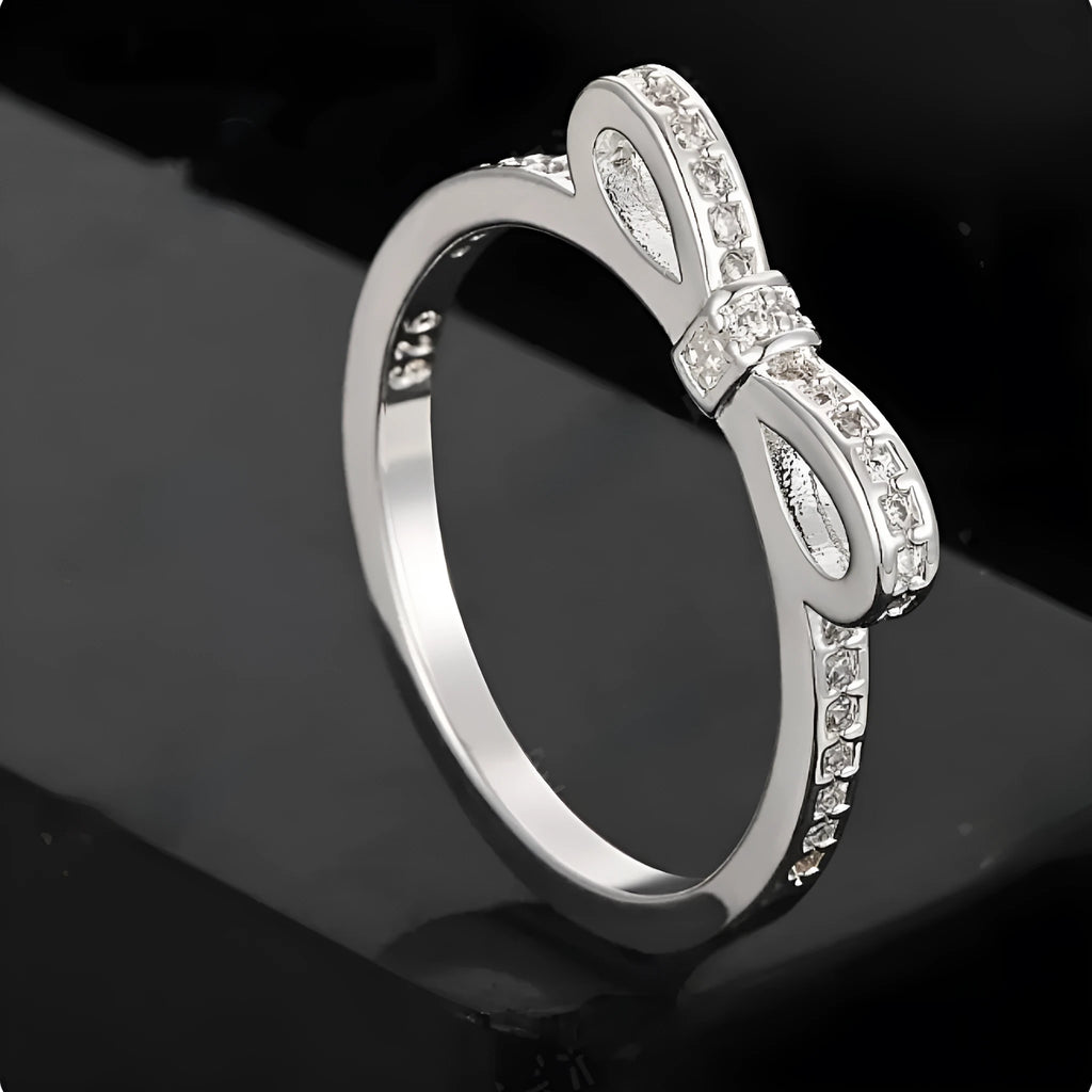 Silver bow-shaped ring with crystal zircon and rhinestone detailing on a finger