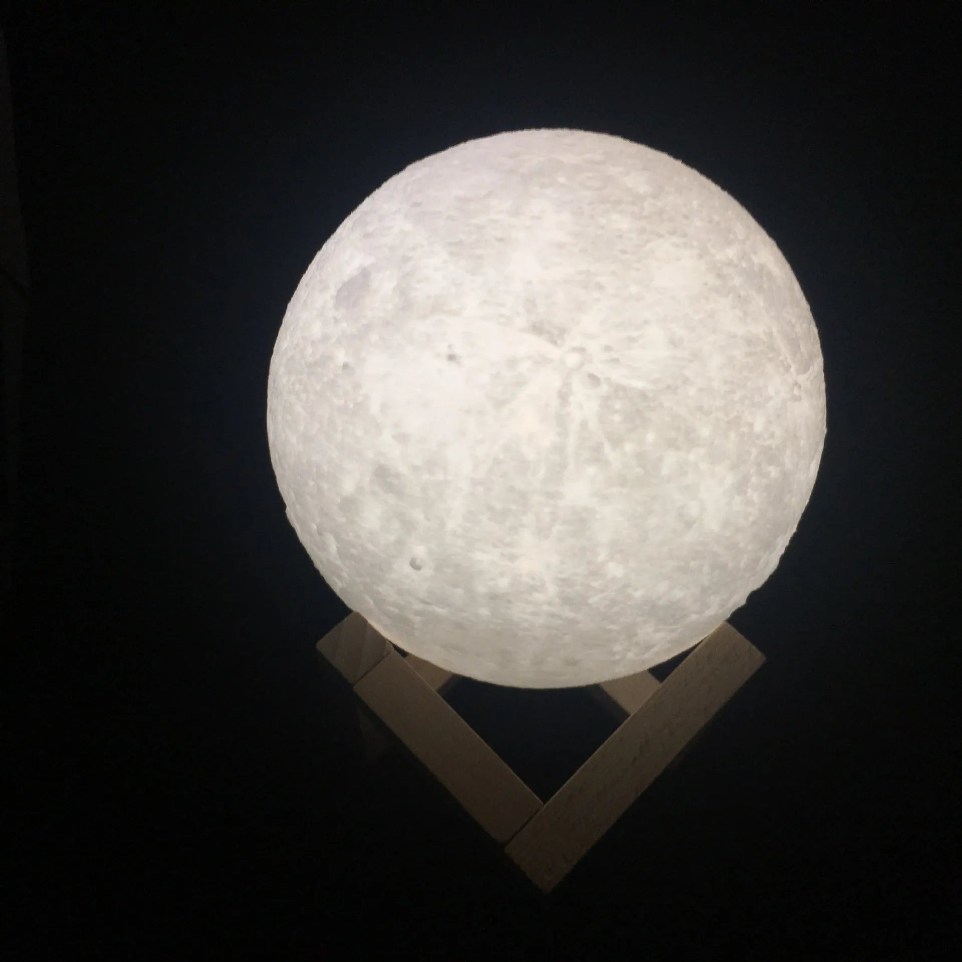 3D printed white moon lamp on a wooden stand with a glowing centre.