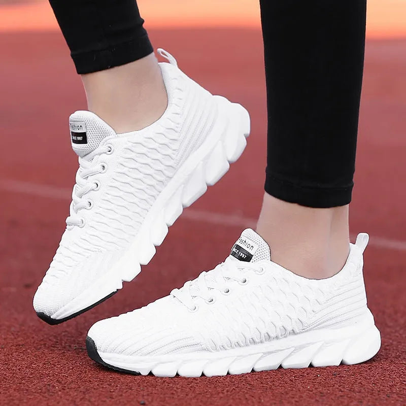 Women's running shoes in black, pink, and white with a fly weave upper and durable outsole.