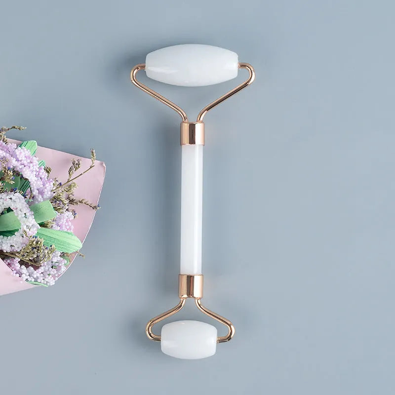 White jade facial roller and Gua Sha scraping board set on a plain surface.