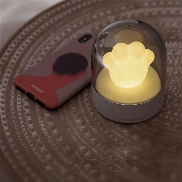 Grey cat paw shaped musical night light with USB charging cable on wooden desktop