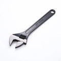 Blackened high carbon steel adjustable open-end wrench on a workbench, jaw set to mid-opening.