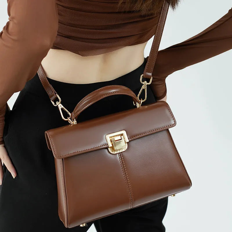 Black leather women's shoulder bag with vachette clasp showing square shape and adjustable strap.